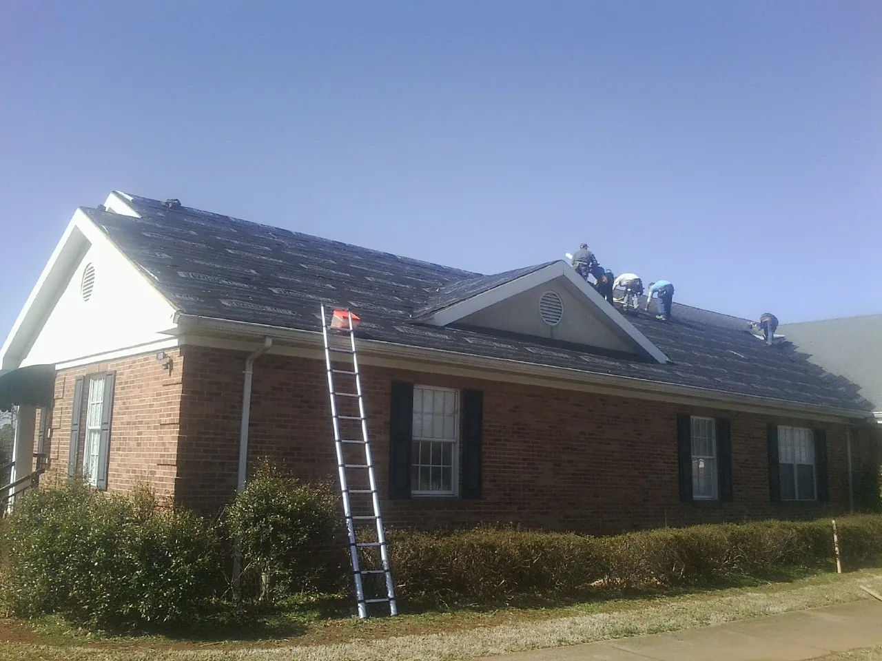 Crew tearing shingles off a brick ranch roof with a ladder set — Emergency Roof Repair work by our crew in Easthampton