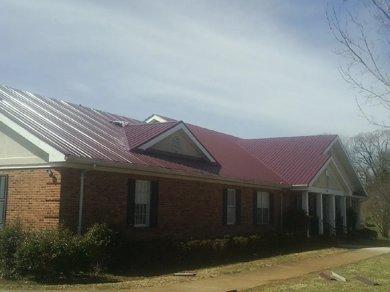Red metal roof with gabled entries on a long brick building, from a Hail Damage Roof Repair job in Easthampton
