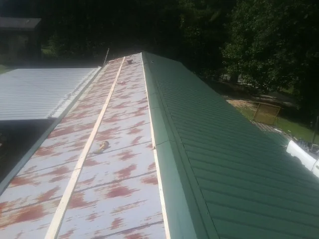 Old rusted panels beside newly installed green metal roofing — Wind Damage Roof Repair by Roofing Brothers in Easthampton