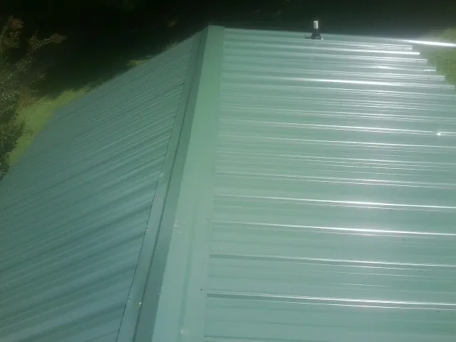 New green metal panels meeting at the ridge of a roof — Flat Roof Repair work by our crew in Easthampton