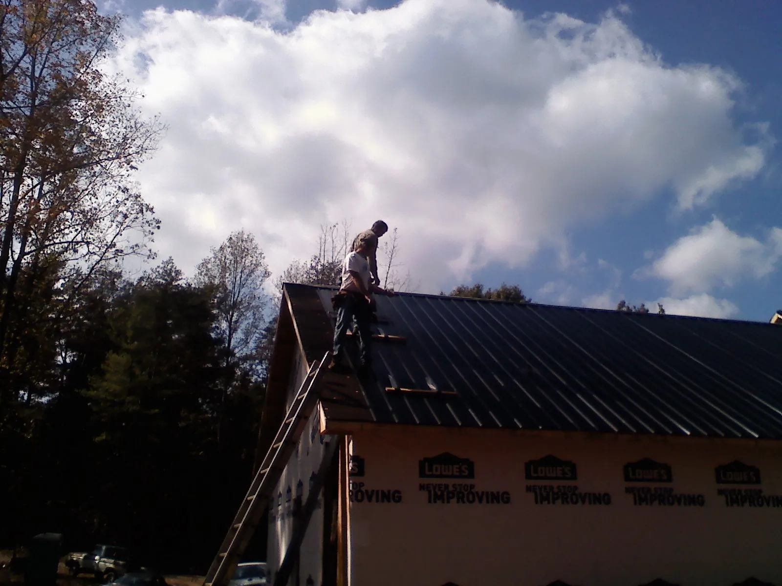 Roofer fastening dark metal panels high against a cloudy sky, from a Roof Inspection job in Easthampton